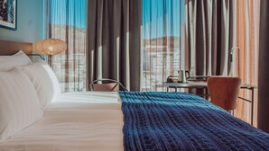 A hotel room with a bed, a chair, a table with a coffee pot, and curtains.