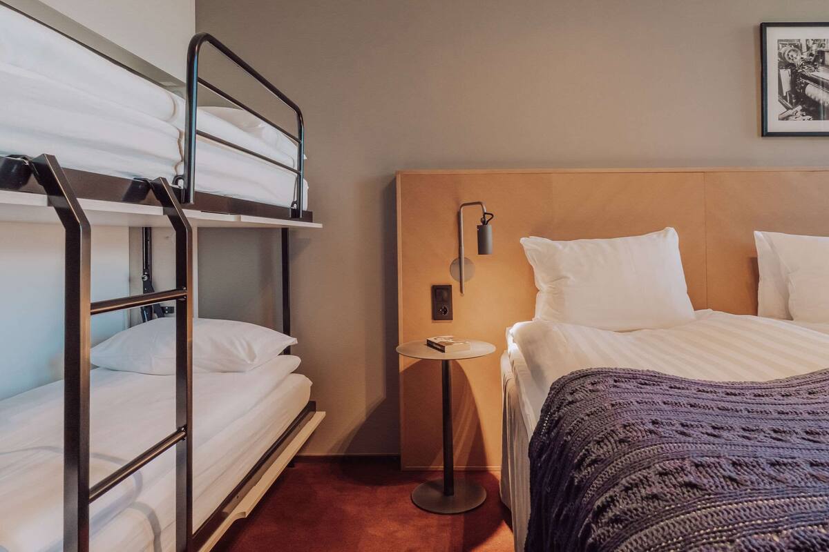Een hotelkamer met stapelbedden, een enkel bed, een ronde tafel en een wandlamp.