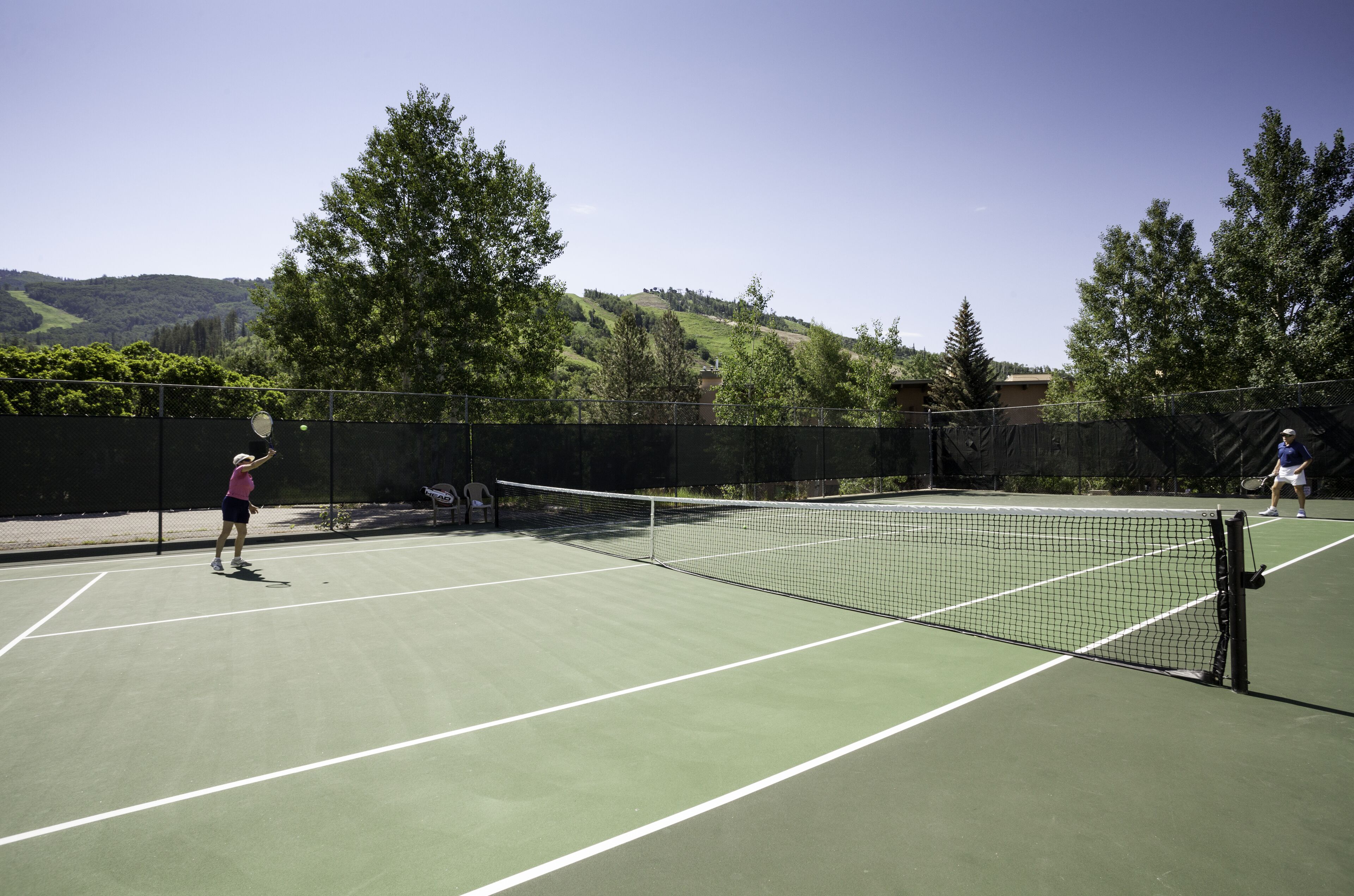A tennis court with a net in the middle, surrounded by a fence and trees.