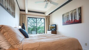 A bedroom with a large bed, a ceiling fan, a window with curtains, a painting on the wall, and a small table with a lamp. - CA117 | Lovely Mountainside Condo | Steps from slopes | Winter Shuttle | Hot Tub (Steamboat Springs)