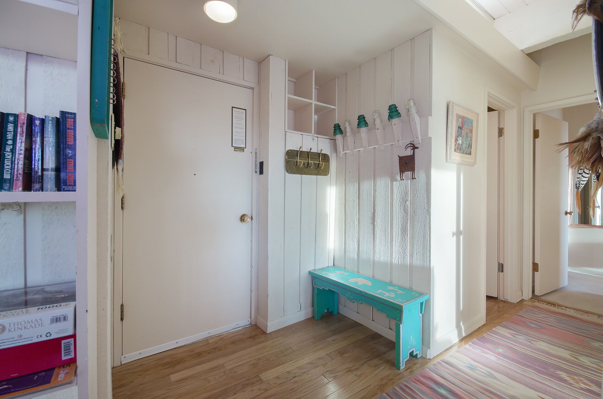 A hallway with a white door, a teal bench, and a bookshelf with books.