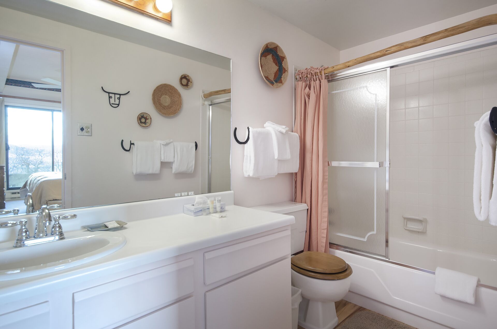 Un bagno con lavandino, mobile lavabo e water bianchi. Asciugamani appesi a ganci e tenda da doccia.