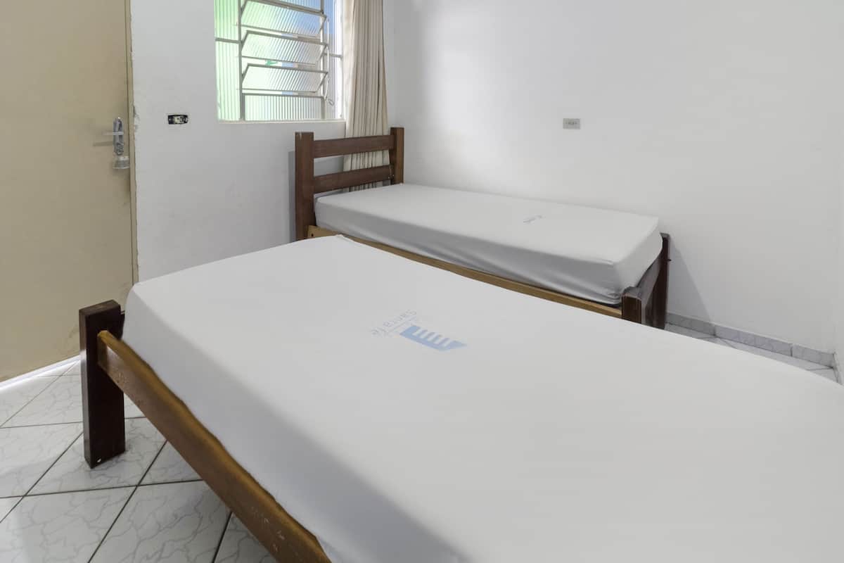 Ein Zimmer mit zwei Einzelbetten, einem Fenster mit Rollläden, einer Tür und einem Fliesenboden.