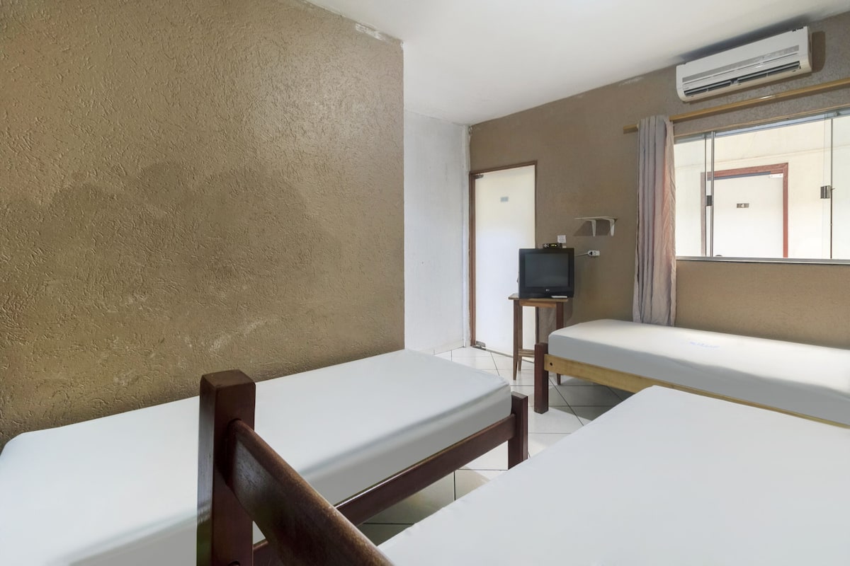 Ein Zimmer mit zwei Einzelbetten, einem Fernseher auf einem kleinen Tisch und einer an der Wand befestigten Klimaanlage.