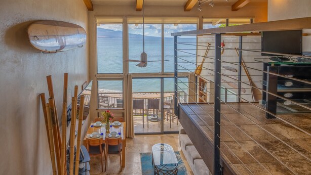 Un interior moderno con comedor, un ventanal con vistas al mar y una escalera que lleva a un balcón.