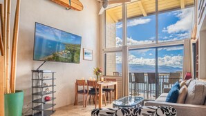 Una sala de estar con televisor grande, una mesa de comedor, sillas, un sofá y un balcón con vista al mar.