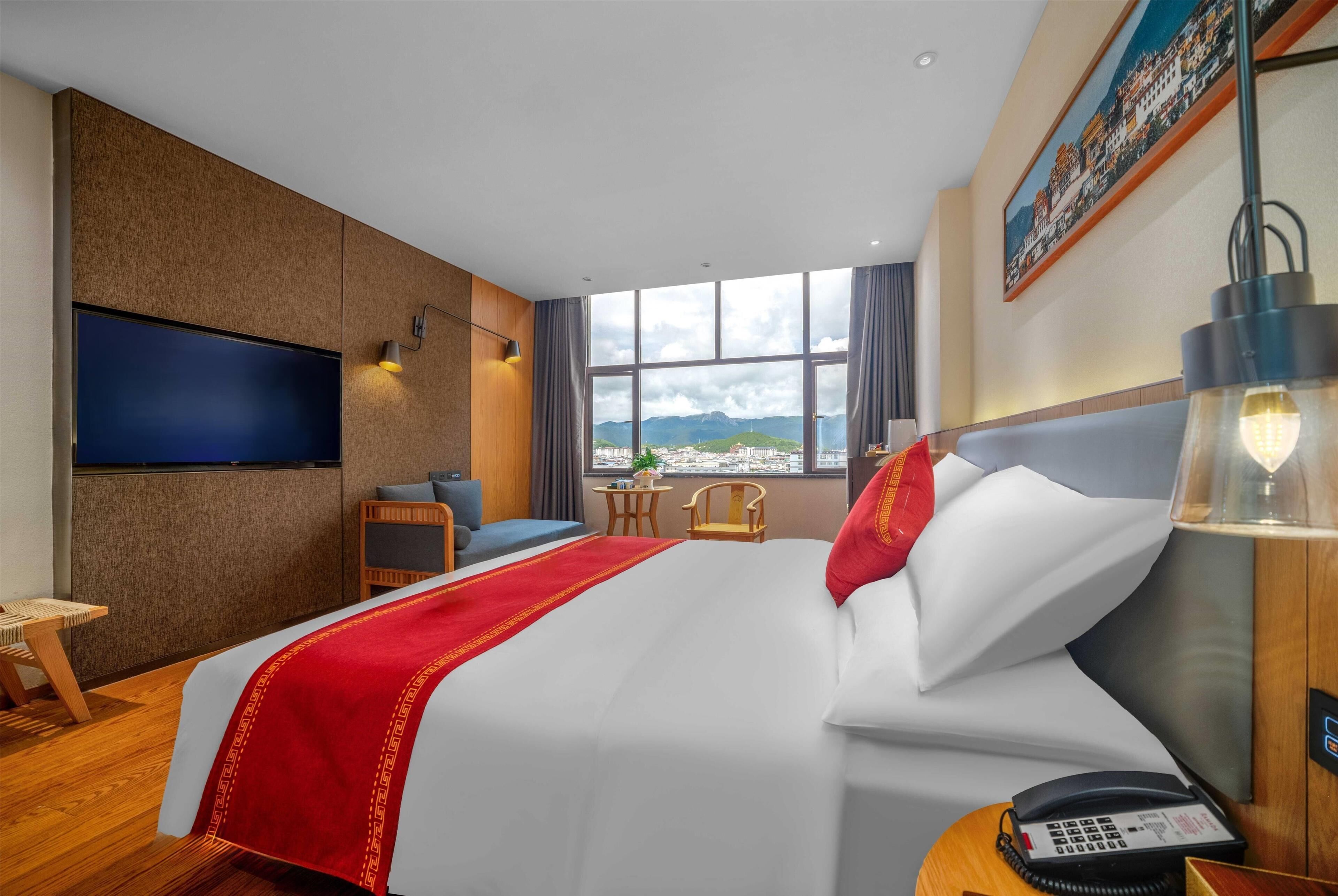 Ett hotellrum med en stor säng, en platt-TV som är monterad på väggen, ett skrivbord med en telefon och utsikt över bergen genom fönstret.
