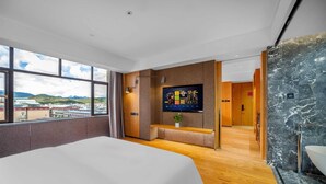 Habitación de hotel moderna con una cama grande, televisor, vistas a la ciudad y un baño de mármol.