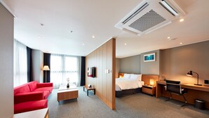Ein modernes Hotelzimmer mit einem roten Sofa, einem Bett, einem Schreibtisch und einem Fernseher.