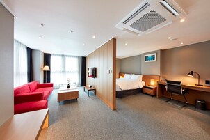 A modern hotel room with a red sofa, a bed, a desk, and a TV.