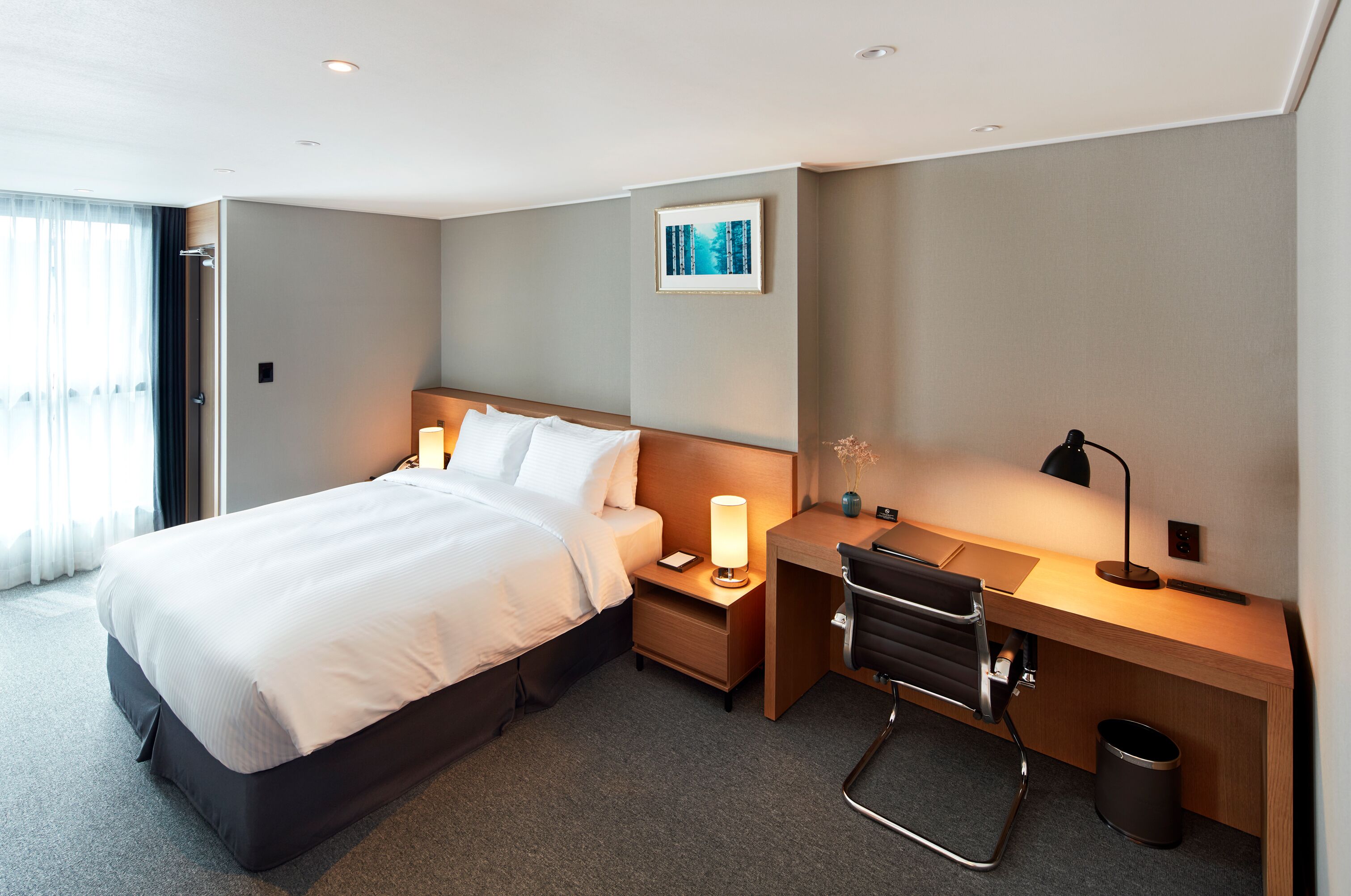 Ein Hotelzimmer mit Bett, Nachttisch, Schreibtisch, Stuhl und Mülleimer.