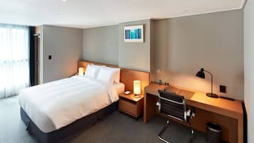 Habitación de hotel con cama, mesita de noche, escritorio, silla y un cubo de basura.
