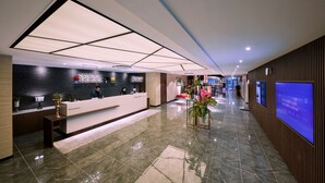 Ein moderner Hotel-Empfangsbereich mit einer Rezeption, einem großen digitalen Bildschirm und einem gut beleuchteten Korridor.