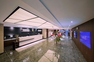 A modern hotel reception area with a reception desk, a large digital screen, and a well-lit corridor.