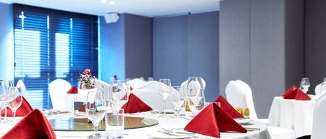 A dining area with round tables set for a meal, white tablecloths, and red napkins.