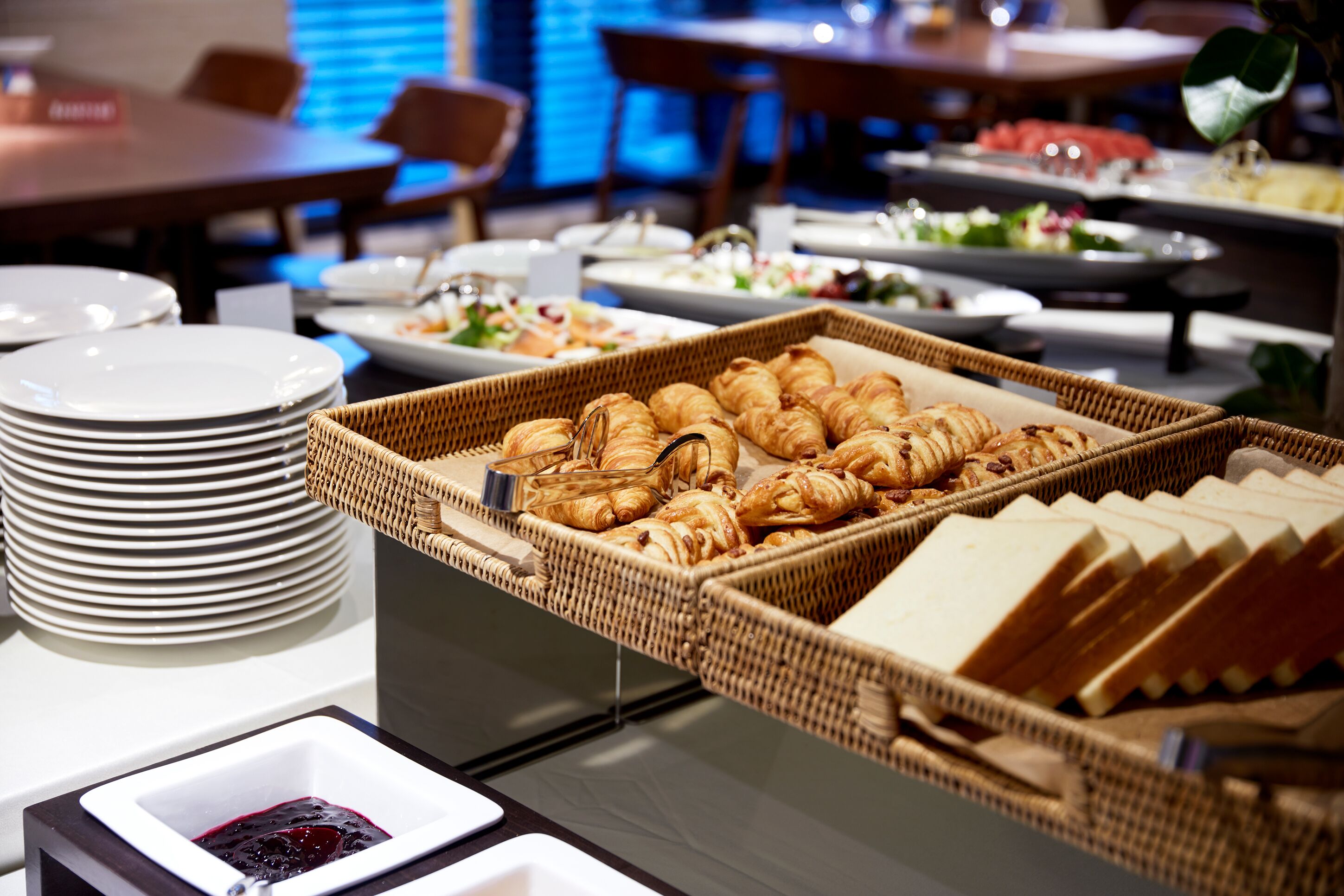 A buffet setup with croissants, bread, and a fruit bowl.