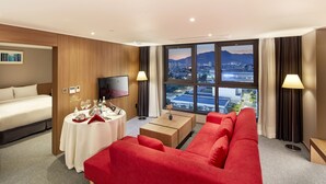 Ein Hotelzimmer mit einem Bett, einem roten Sofa, einem kleinen Tisch mit einem Fernseher und einem großen Fenster mit Blick auf die Stadt.