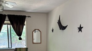 Un dormitorio con cama, cómoda de madera, espejo y adornos en la pared como estrellas y una luna creciente.