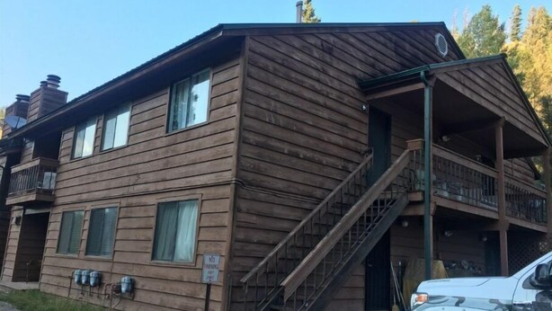 Eine zweistöckige Holzhütte mit einem Balkon im zweiten Stock, einer Treppe zum Eingang und einem geparkten Fahrzeug davor.