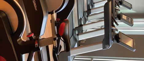 A row of stationary bikes in a gym with a window in the background.