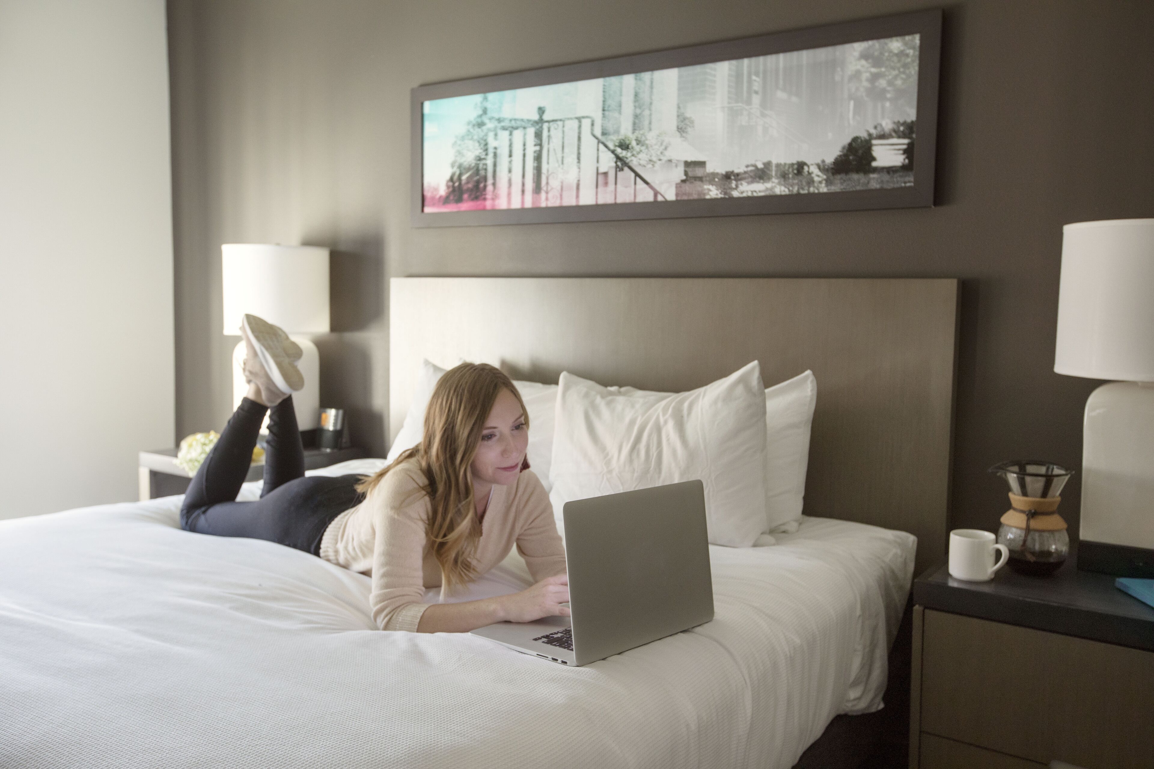 Una habitación de hotel con una cama, una computadora portátil, un fabricante de café y un cuadro en la pared.