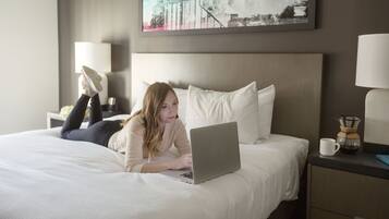Una habitación de hotel con una cama, una computadora portátil, un fabricante de café y un cuadro en la pared.
