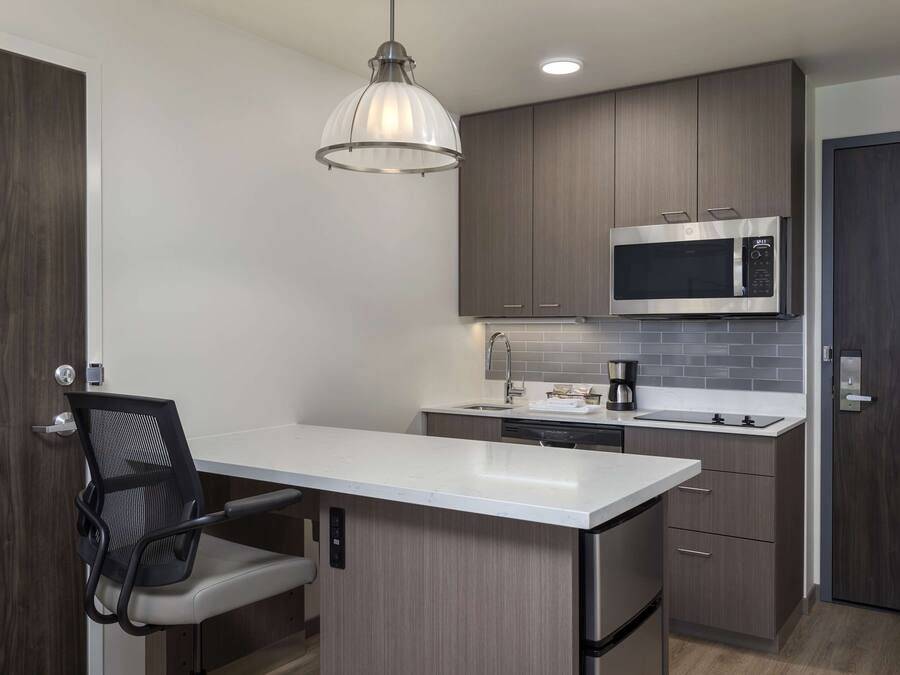 A compact kitchen with a microwave, sink, and a chair.
