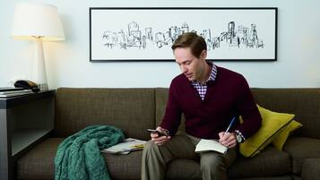 A person sitting on a couch with a lamp, a framed cityscape, and a notebook.