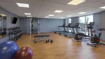 Une salle de sport équipée de tapis de course, de vélos elliptiques, de poids libres et de ballons d’exercice.