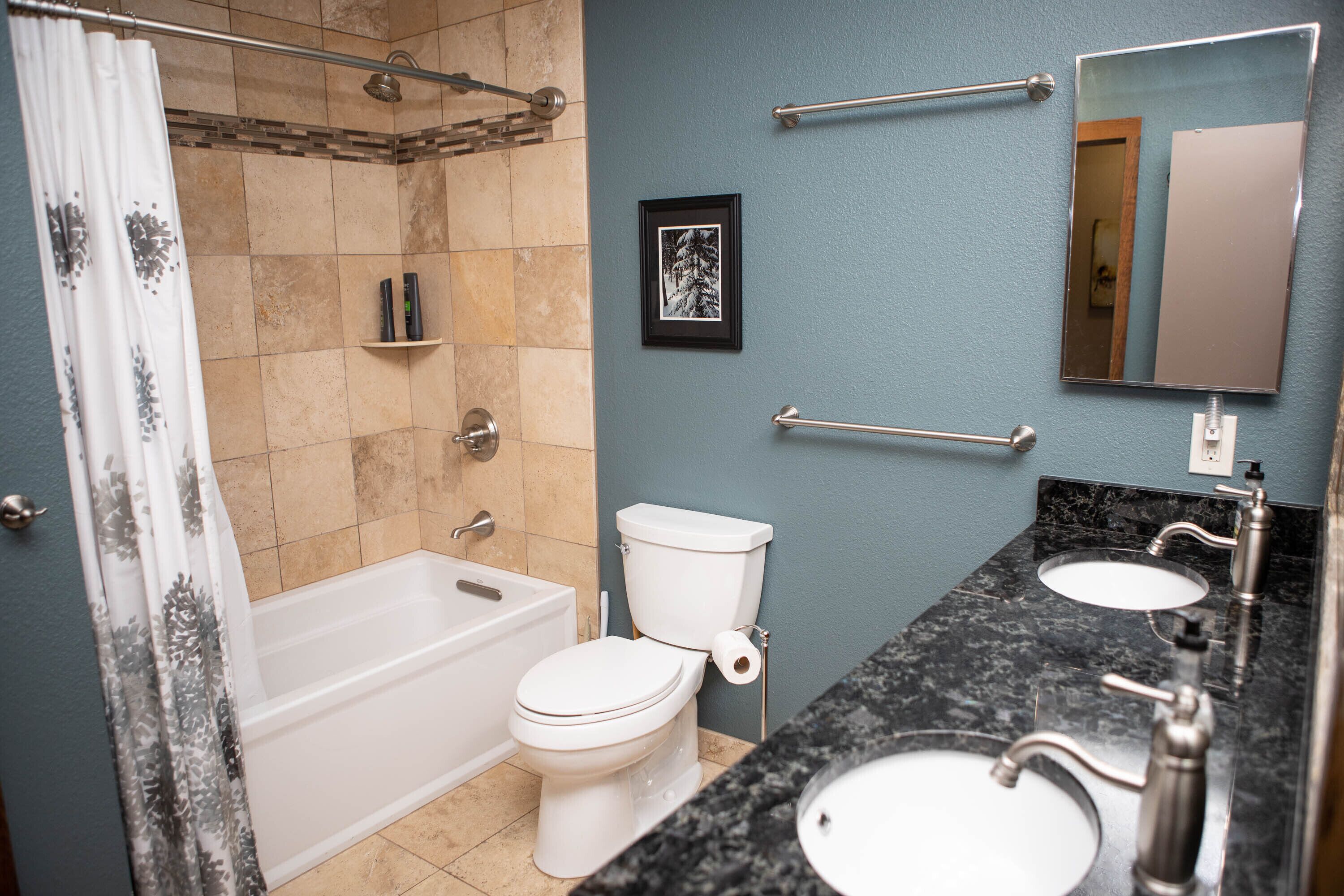 A bathroom with a bathtub, toilet, two sinks, and a shower curtain.