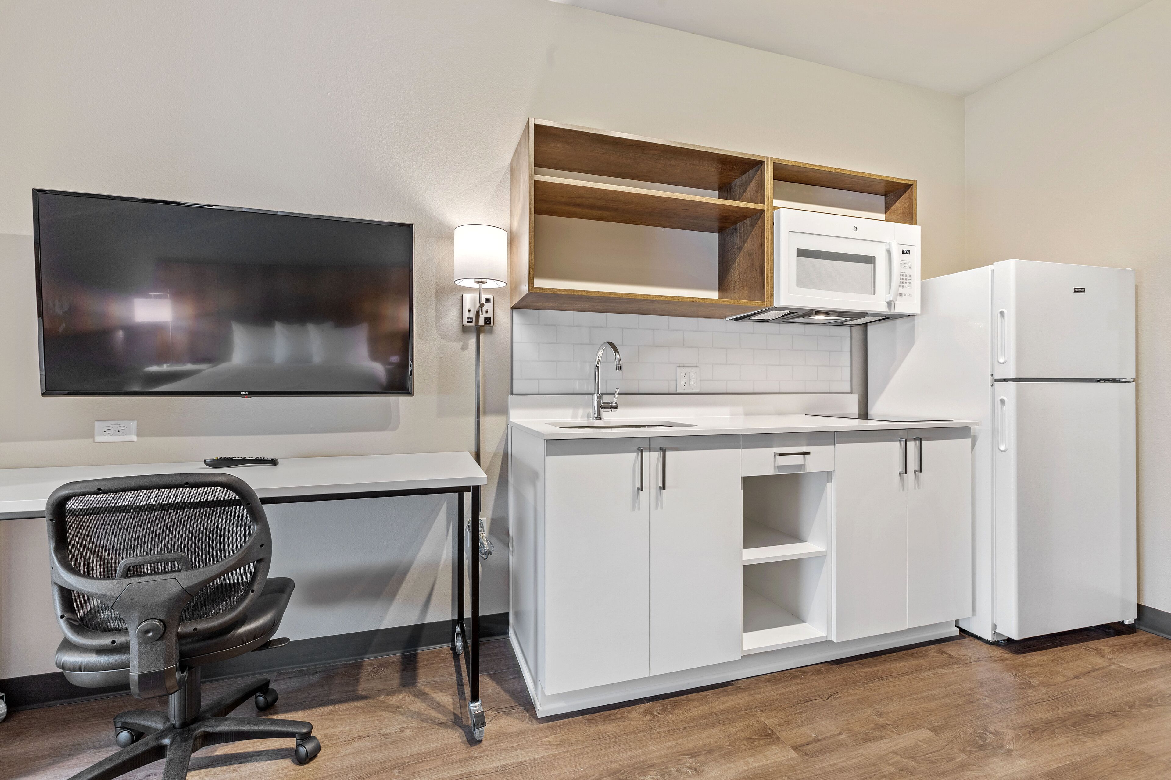 Eine moderne Küche mit weißen Schränken, einer Mikrowelle, einem Kühlschrank und einem an der Wand montierten Fernseher.