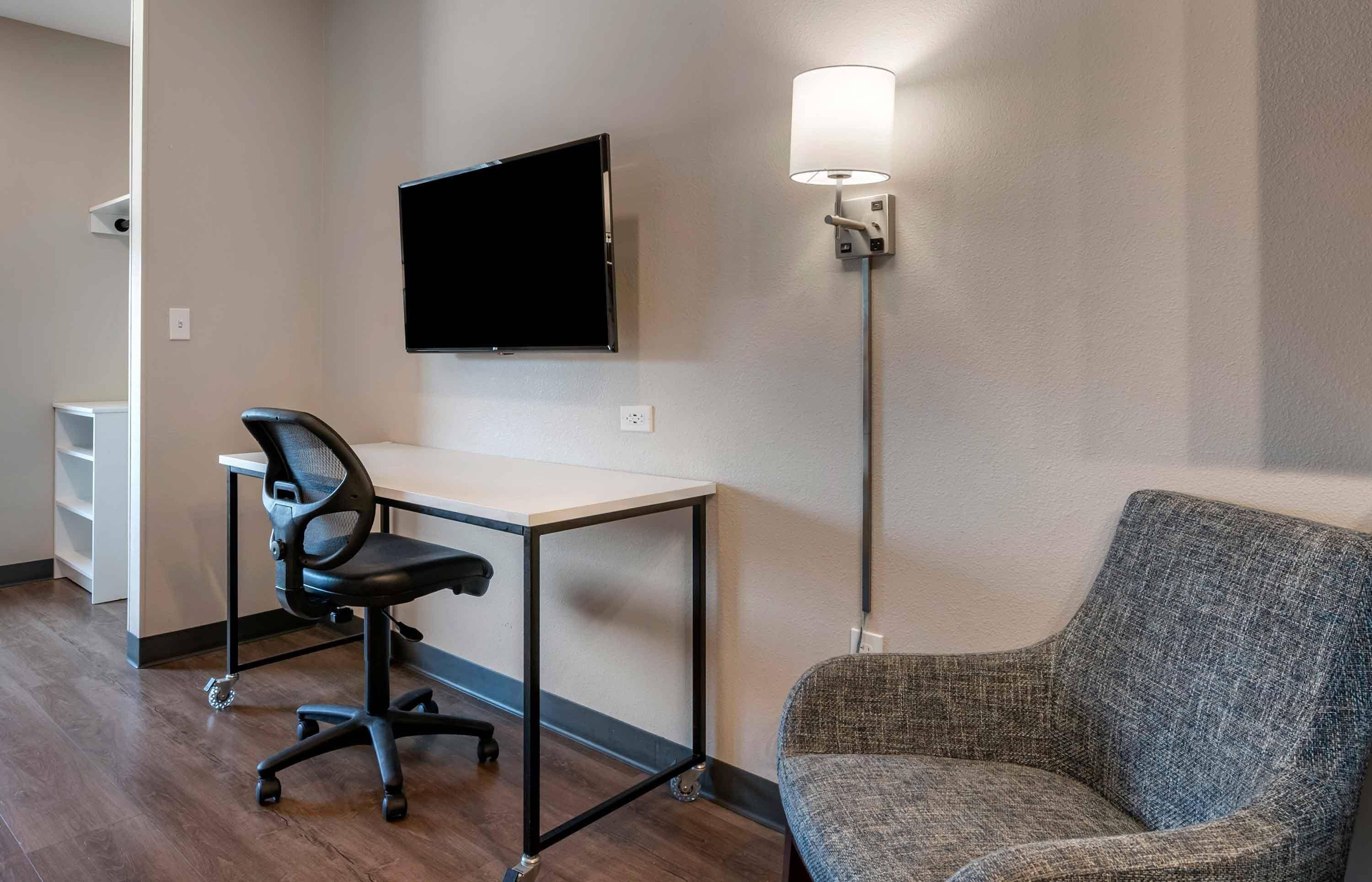 Habitación de hotel con escritorio, silla, televisor de pantalla plana y lámpara de pie.