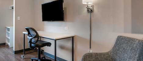 Habitación de hotel con escritorio, silla, televisor de pantalla plana y lámpara de pie.