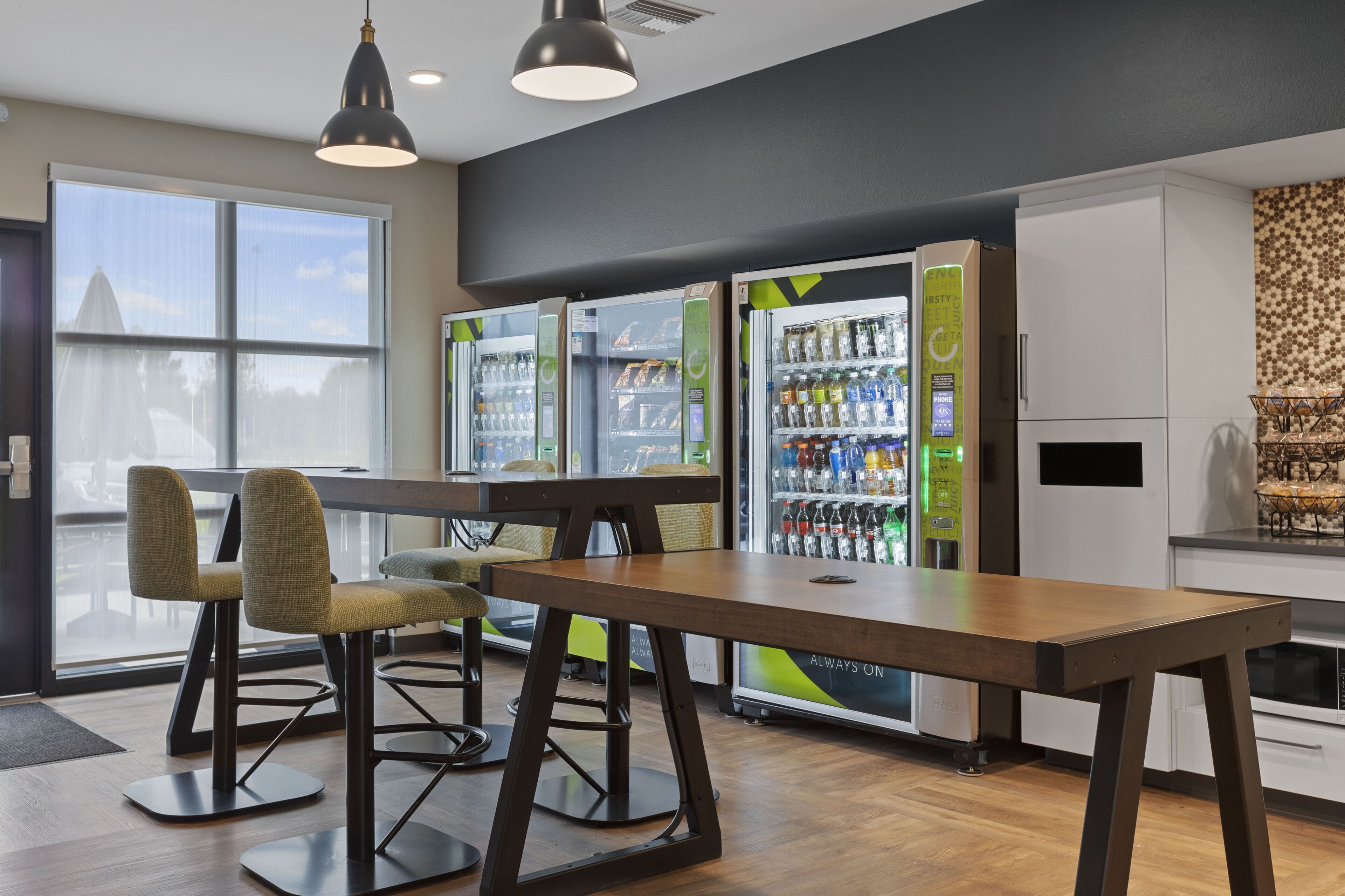 A modern interior with a wooden table and chairs, vending machines, and a kitchen area.