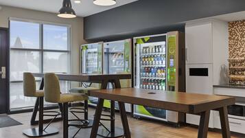 A modern interior with a wooden table and chairs, vending machines, and a kitchen area.