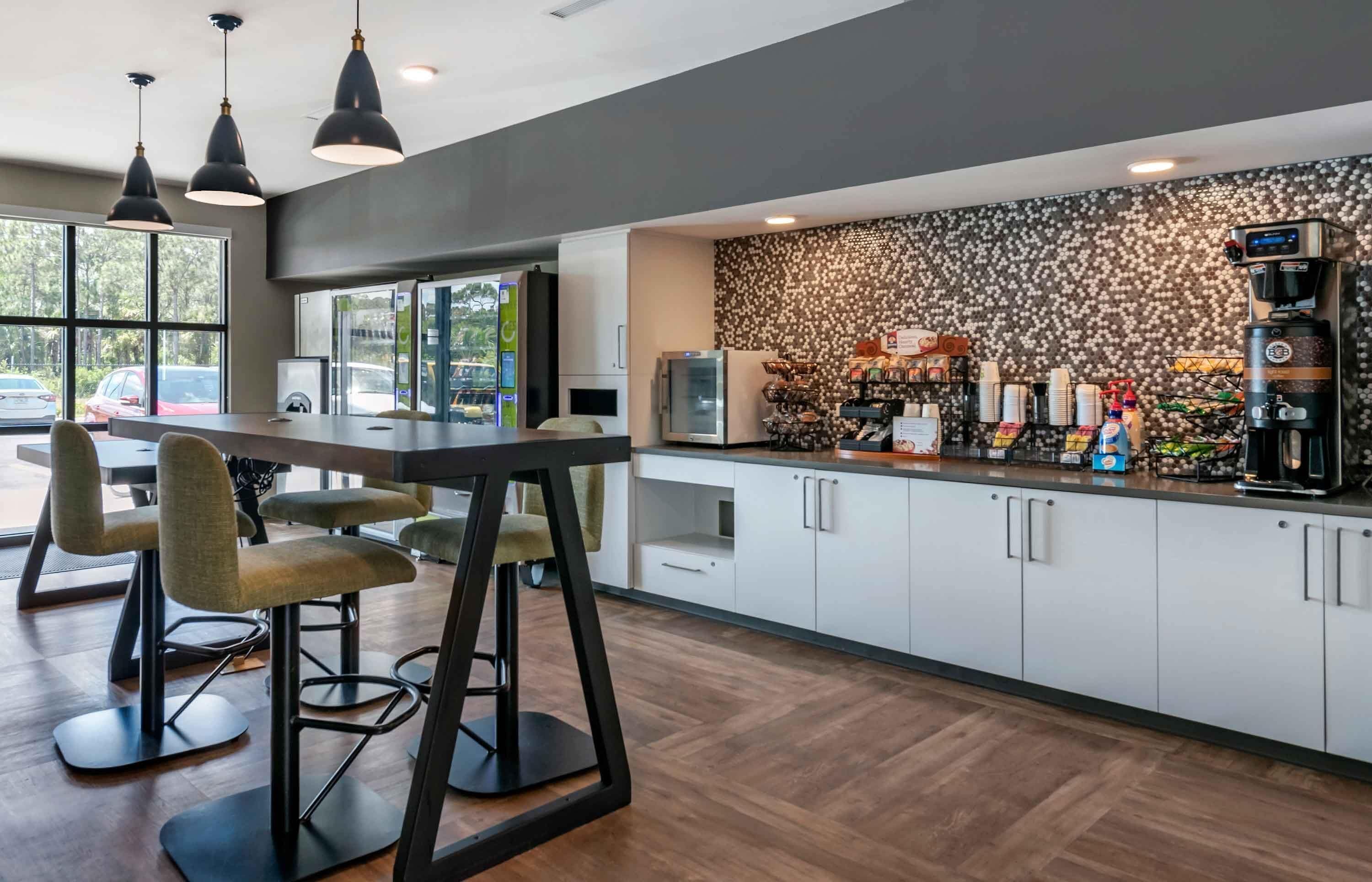 A modern kitchen with a bar area, bar stools, a coffee machine, and a patterned backsplash.