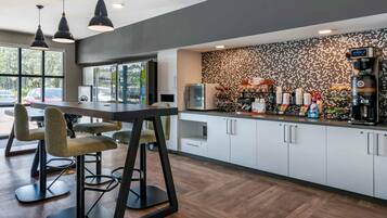 A modern kitchen with a bar area, bar stools, a coffee machine, and a patterned backsplash.