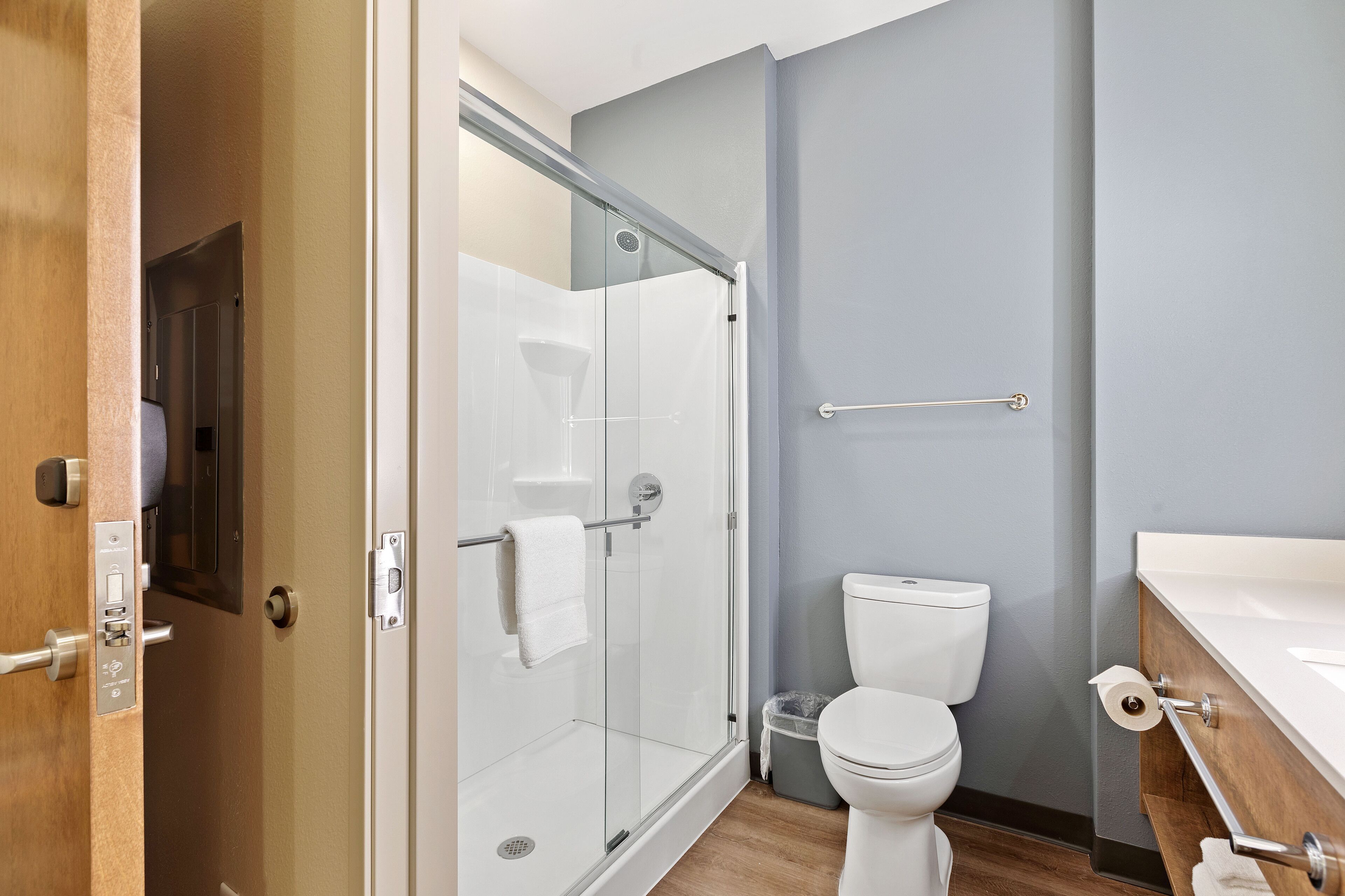 Un baño moderno con cabina de ducha de vidrio, inodoro blanco y tocador de madera.