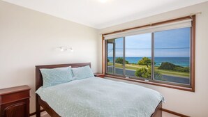 Een slaapkamer met een groot raam dat uitzicht geeft op de oceaan en een weg.
