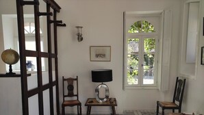 A room with a patterned floor, a wooden chair, a table with a lamp, a globe, and a window with a view of greenery. - Gîte Rohan - Château du Parc Soubise (Mouchamps)