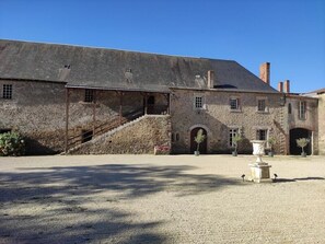 Un bâtiment historique en pierre, doté d’un escalier couvert, d’une cour et d’une fontaine.