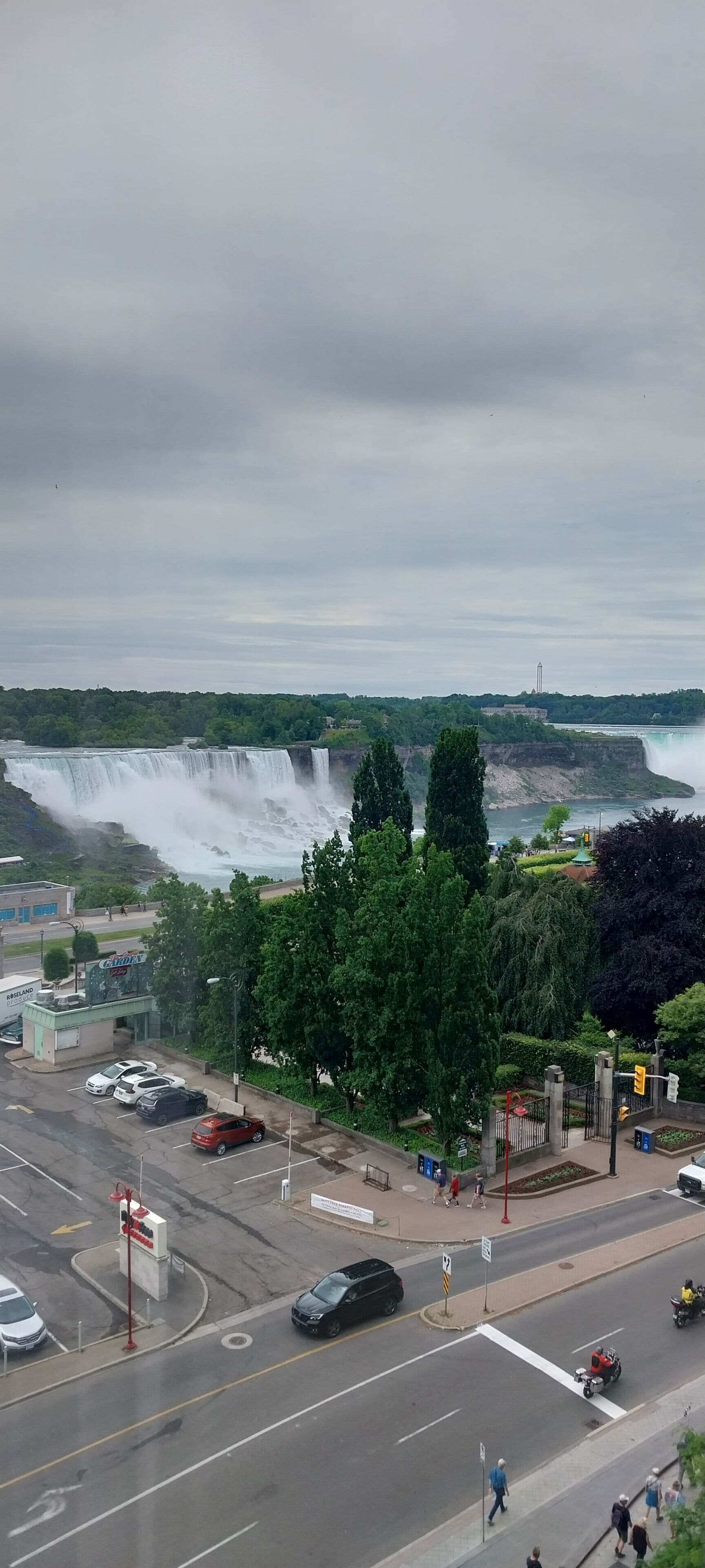 A view of a waterfall and a parking area with cars and pedestrians.