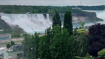 A view of a waterfall and a parking area with cars and pedestrians.