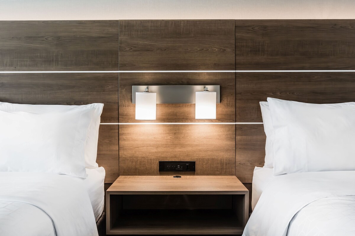 A hotel room with two beds, a wooden headboard, and a bedside table with a built-in light.