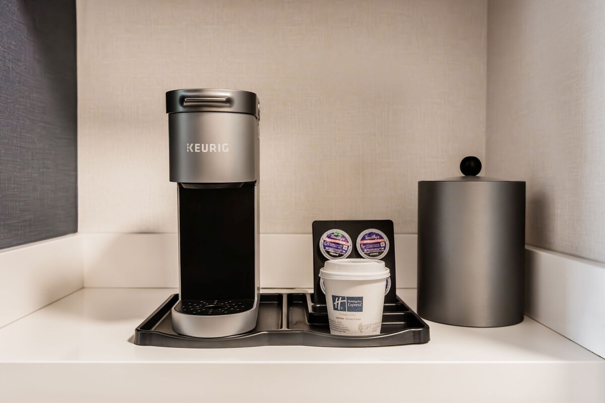 A Keurig coffee maker on a tray with a coffee cup and two Keurig pods.