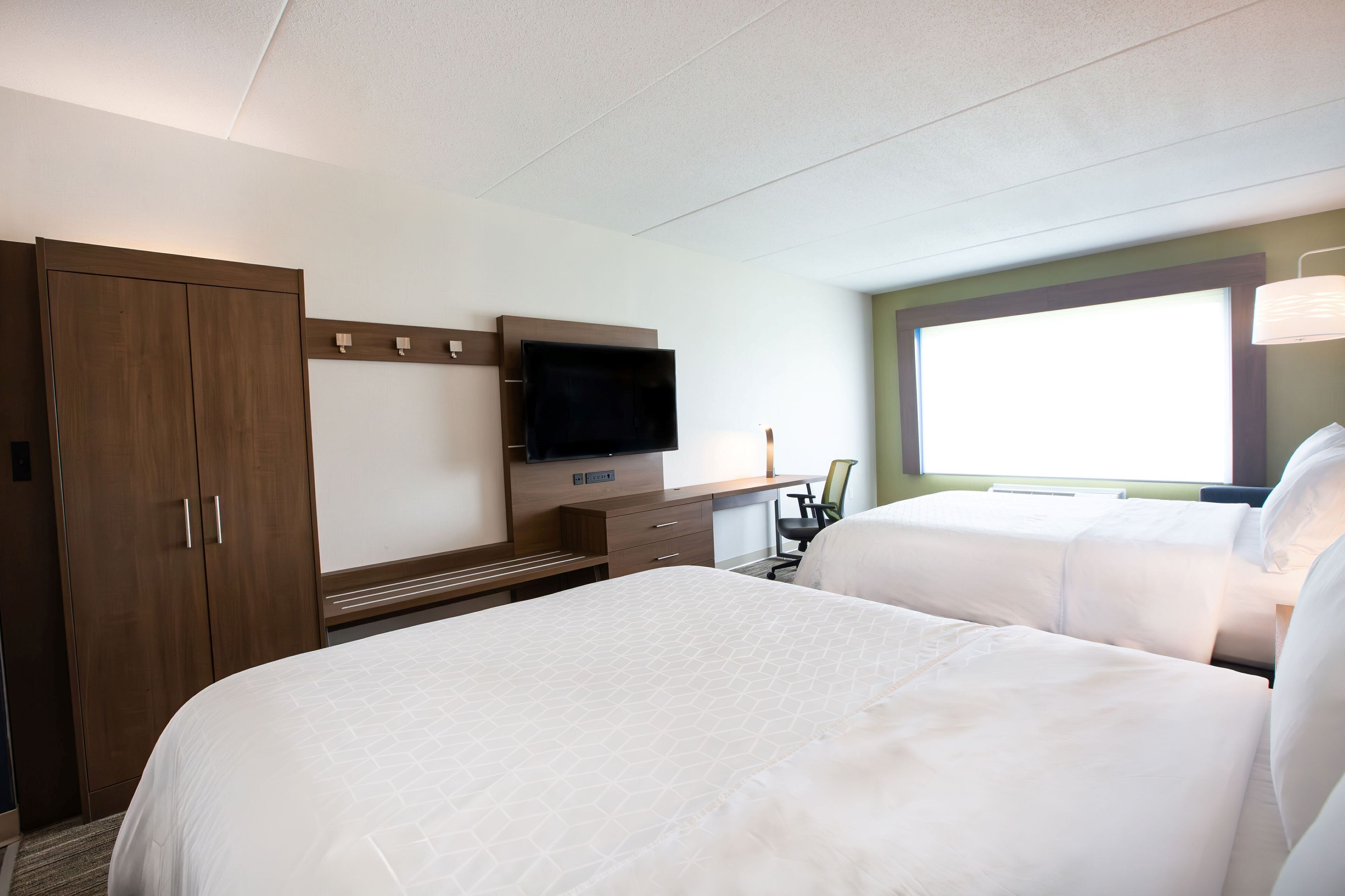A hotel room with two beds, a TV, a desk, and a window.