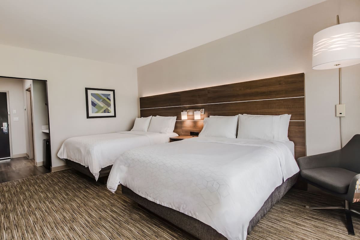 A hotel room with two beds, a desk, a chair, a lamp, and a painting on the wall.