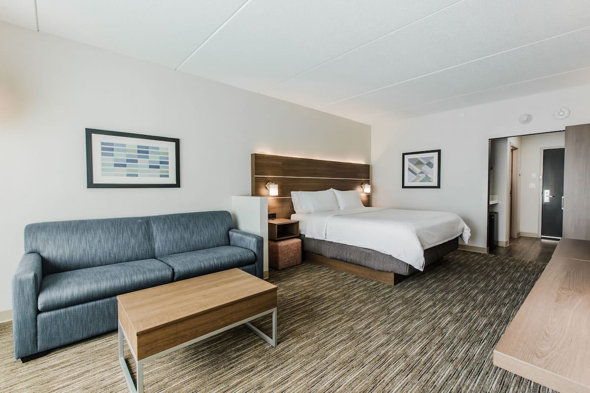 A hotel room with a bed, a sofa, a wooden coffee table, and a carpeted floor.