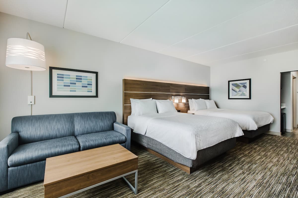 A modern hotel room with a large bed, a sofa, and a wooden coffee table.