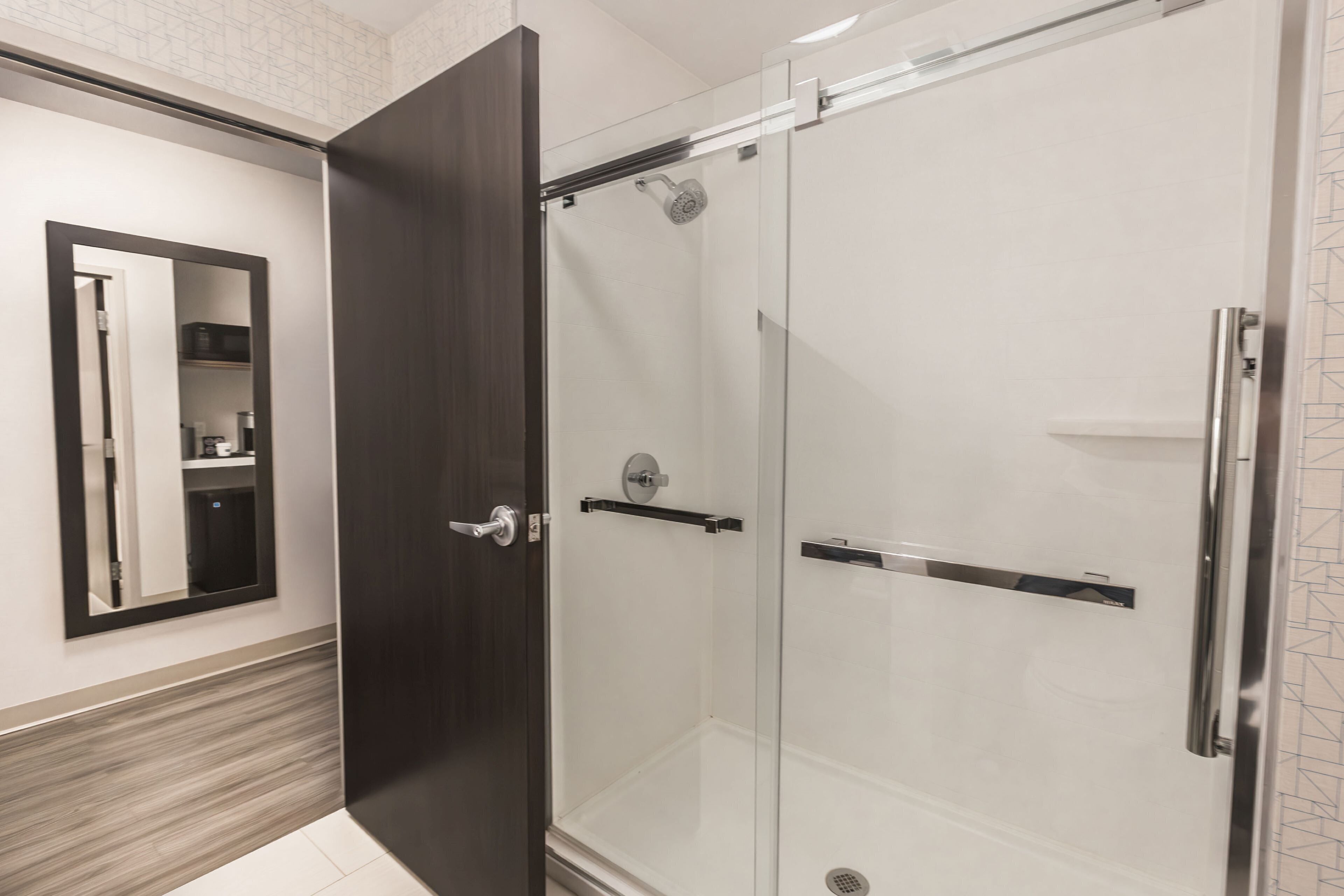 Un baño moderno con ducha envuelta en cristal, una puerta de madera oscura y una pared espejada.